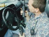 A police officer sitting in a vehicle holding multiple portable radios.